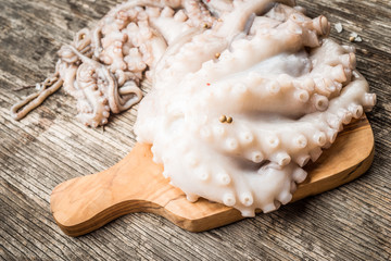Whole raw octopus on cutting board on rustic wooden table