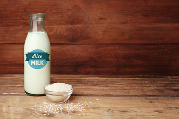 Bottle of milk and little bowl with rice on wooden background