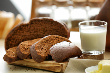 Wooden board with cut bread and glass of milk on kitchen table