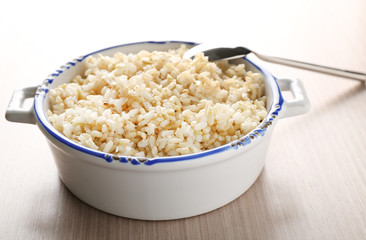 Modern ceramic saucepan full of boiled brown rice on wooden table