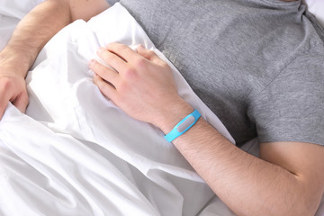 Young man with sleep tracker resting in bed at home, closeup