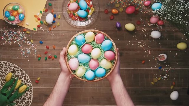Man holding a basket with easter eggs in front of table decorated with easter eggs. Top view