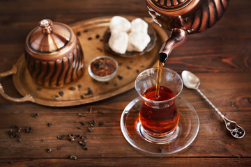 Poring Turkish tea into traditional glass on wooden table closeup
