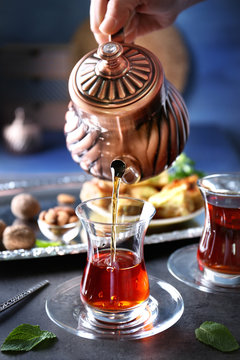 Female hand pouring Turkish tea into traditional glass on table closeup