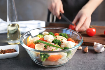 Woman preparing chicken with vegetables in glass bowl