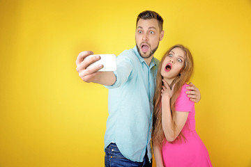 Funny young couple taking selfie on color background