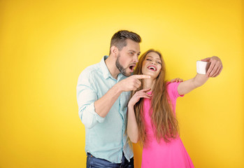 Funny young couple taking selfie on color background