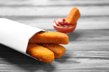 Paper bag with cheese sticks and ketchup sauce on wooden background