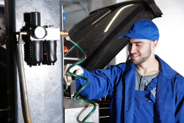 Young mechanic standing near auto lift in car service