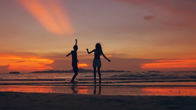 Slow motion silhouette of happy loving couple meet and play at the beach on sunset in ocean shore
