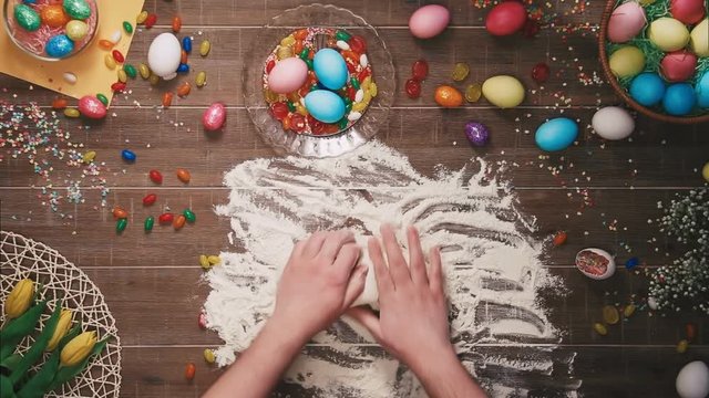 Man kneading dough on table decorated with easter eggs. Top view