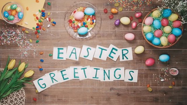 Man puts words Easter Geetings on table decorated with easter eggs. Top view