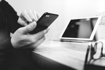 businessman hand using smart phone,mobile payments online shopping,omni channel,digital tablet docking keyboard computer in modern office on wooden desk,black and white