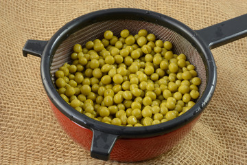 Canned sweet peas draining in strainer in bowl to lower salt content