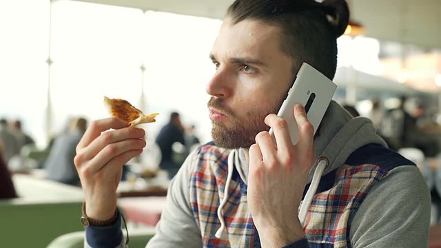 Hipster eating pizza in bistro and chatting on cellphone, steadycam shot
