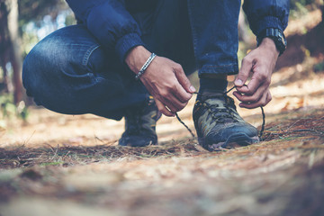 Young hiker man ties the laces on his shoe during a holiday backpacking in forest.