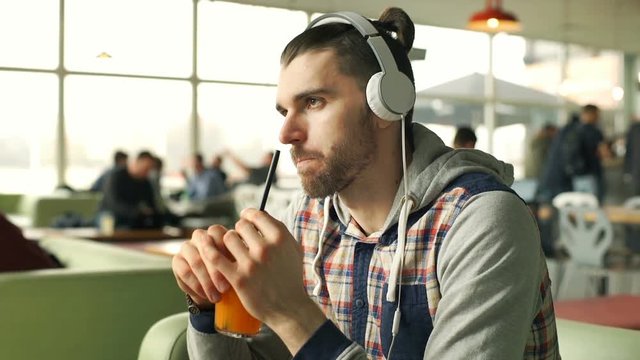 Relaxed man listening music on headphones and drinking juice in the cafe, steadycam shot
