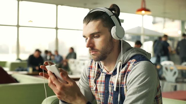 Happy man listening music on headphones and browsing internet on smartphone, steadycam shot
