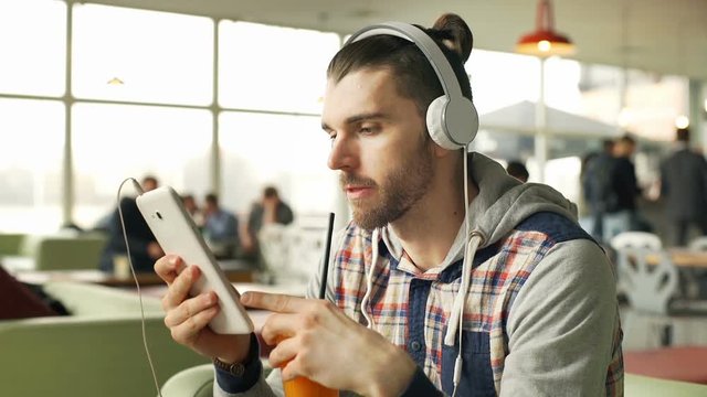 Absorbed man listening music on headphones in the cafe and drinking juice, steadycam shot
