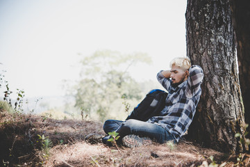 Portrait of young beard man sitting alone by a tree with backpack looking away enjoy with nature.
