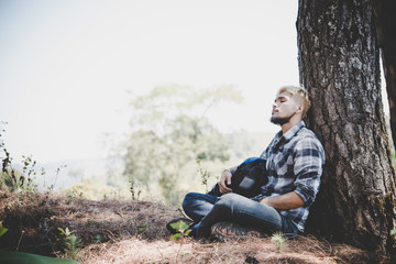 Portrait of young beard man sitting alone by a tree with backpack looking away enjoy with nature.