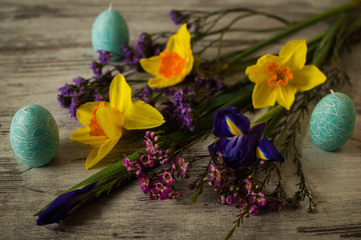 Easter decoration. Candles in the form of Easter eggs on a whigt wooden background. A wonderful bouquet of spring flowers and pussy-willow branch.