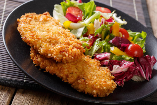 Chicken cutlet in a breaded and fresh mix of salad close-up. horizontal