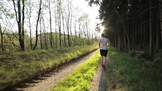 Mann in Sportkleidung l&auml;uft bei Sonnenuntergang im Gras und Kiesel Richtung Sonne