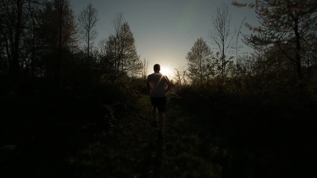 Mann in Sportkleidung l&auml;uft bei Sonnenuntergang im Gras und Kiesel Richtung Sonne