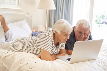 Happy senior couple lying on their bed using a laptop