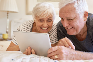 Smiling senior couple using a digital tablet together in bed