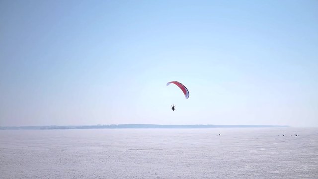 The paraglider hovers like a bird over frozen lakes, and rises up to the blue sky. Slow motion. 1920x1080.