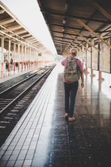 Young hipster man walking through train station. Man waiting for the train at platform. Travel concept.