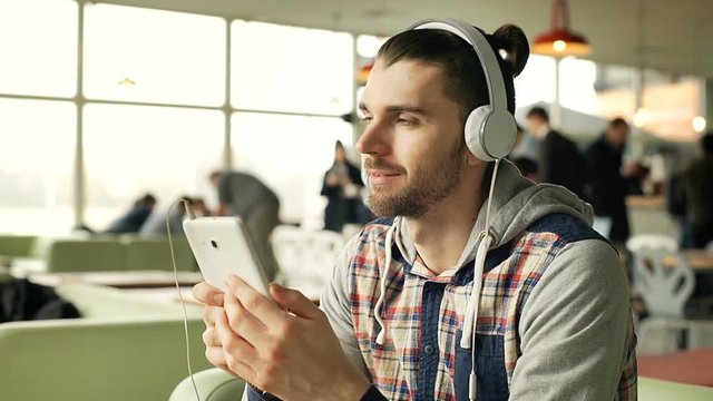 Happy man listening music on headphones and browsing internet on tablet, steadycam shot
