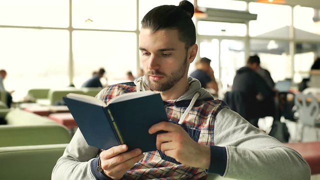 Man receives message on smartphone while reading book in the cafe, steadycam shot

