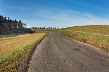 Fototapeta na wymiar Old rural asphalt road in the Czech Republic. Granite road bollard. Agricultural landscape.