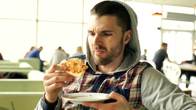 Man in hood looks dissatisfied while eating tasteless pizza, steadycam shot
