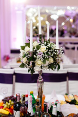Tall silver candleholder decorated with white roses stands on dinner table