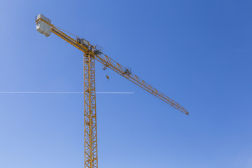 Fototapeta na wymiar high crane on clear blue sky with a passing aircraft
