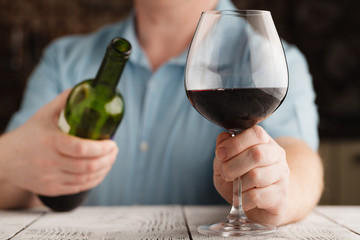 man holding a glass with red wine and bottle