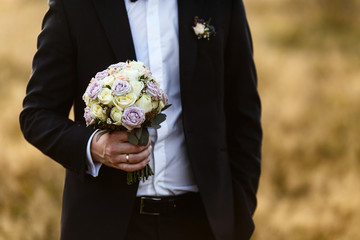 Groom holds in his strong arm violet wedding bouquet