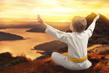 Little boy karate meets the sunrise in the mountains,meditation, training in the mountains.Japanese martial art. The winner of the athlete. © Denis