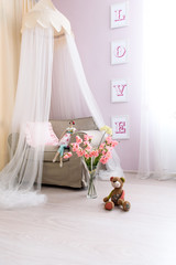 Fototapeta na wymiar View of room design for girl. A gently pink colored room, a comfortable armchair with a canopy above it, pink flowers and a lovely doll, huge love letters on the wall.