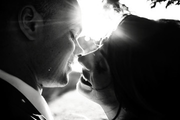 Sun shines over newlyweds' heads while they smile to each other before a kiss