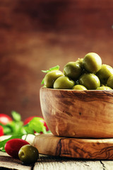 Green olives in a wooden bowl, selective focus