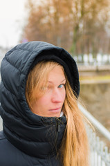 Portrait of a beautiful blonde in a black hood in the winter on the street