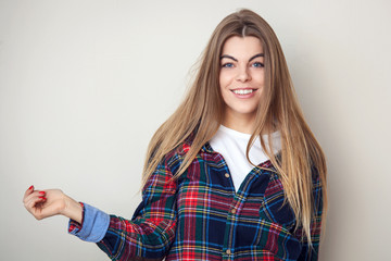Happy young woman in plaid shirt posing against wall.