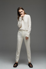 Fashion style model in white sweater and pants, posing in the studio