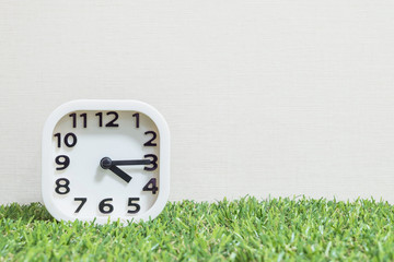 Closeup white clock for decorate show a quarter past four o'clock or 4:15 p.m. on green artificial grass floor and cream wallpaper textured background with copy space