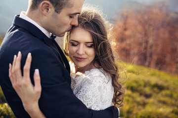 Dreamy bride closes her eyes leaning to groom's chest on spring hill